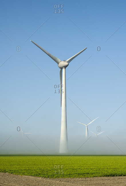 Offshore wind turbines standing in fog on the IJsselmeer inland sea, land based turbines in the clear, Flevoland, Netherlands