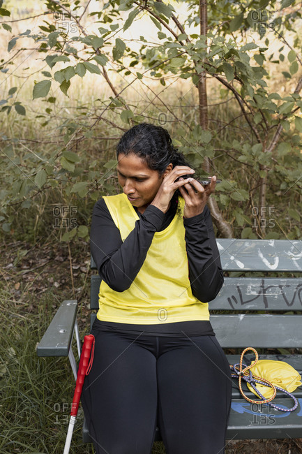 Visually impaired woman sitting on bench and using cell phone