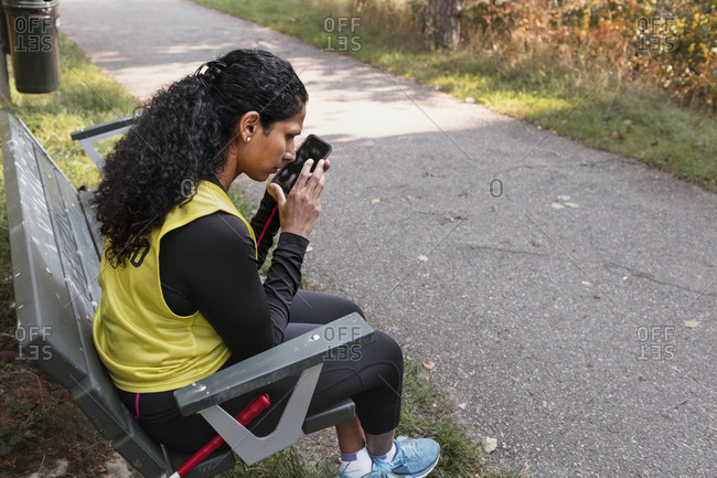 Visually impaired woman sitting on bench and using cell phone