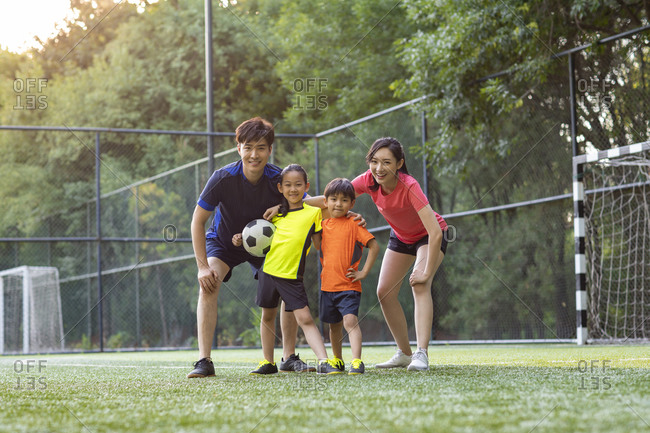 Happy young family playing football on soccer field