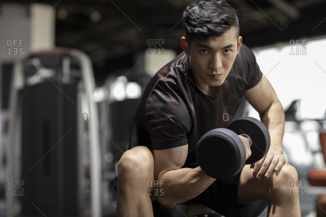 Young man working out with dumbbell at gym