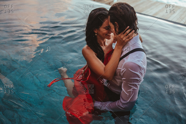 Couple holding each other in arms standing in a swimming pool at a tourist resort. Couple in love on a romantic vacation having fun in a pool at a luxury destination.