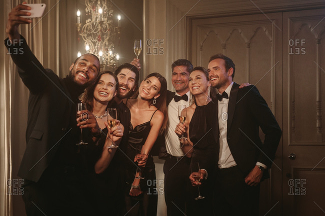 Man taking selfie with his friends at party. Group of men and women raising a toast and posing for a selfie at celebration event.
