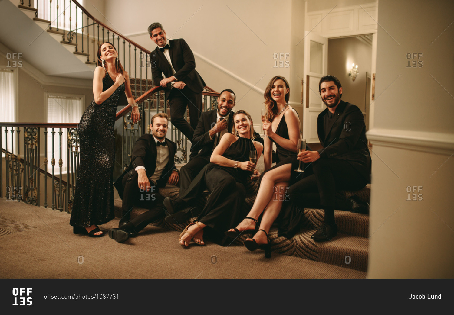 Multi-ethnic group of men and woman sitting at stairs and looking at camera. Large group of socialites enjoying at gala night.