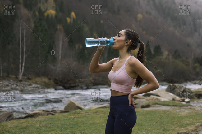 Exhausted young woman drinking water while standing with hand on hip- Ordesa National Park- Huesca- Spain