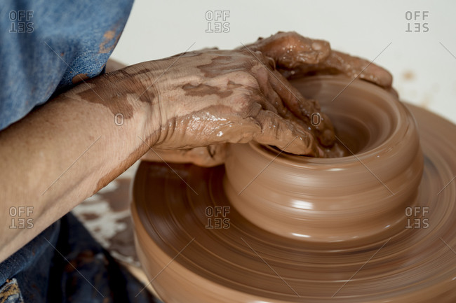 Mature female potter making pottery on wheel at ceramic workshop