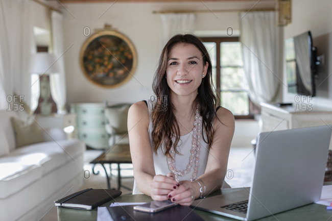 Smiling female event planner sitting by laptop at home