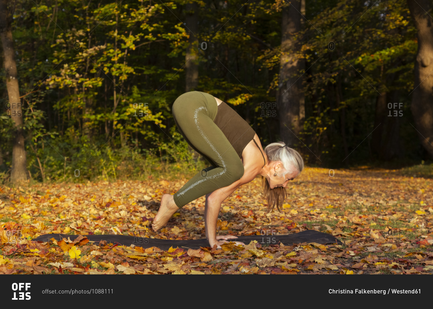 Active mature woman practicing crow pose yoga at park