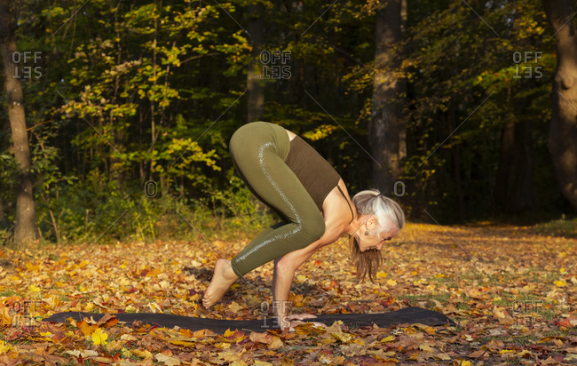 Active mature woman practicing crow pose yoga at park