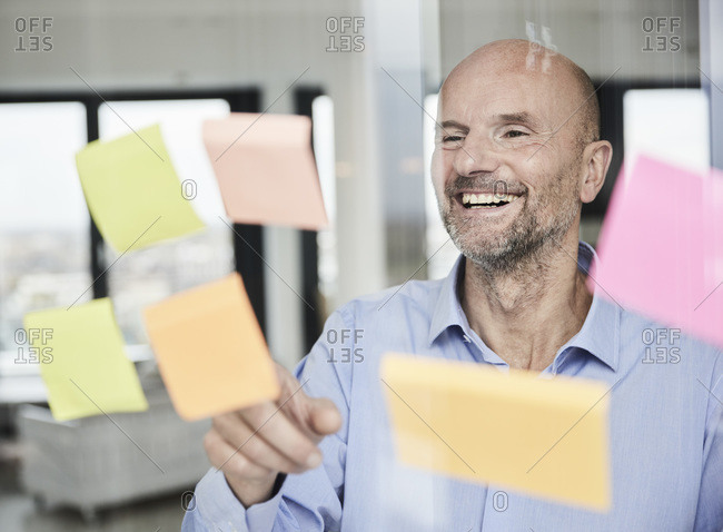 Smiling businessman reading adhesive note on glass wall