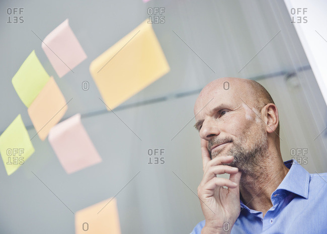 Thoughtful businessman reading adhesive note while standing by glass wall