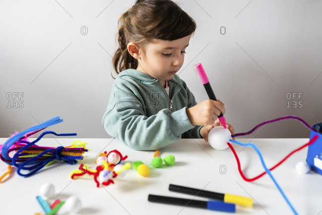 Cute girl making creative toys from pipe cleaners and styrofoam ball at table