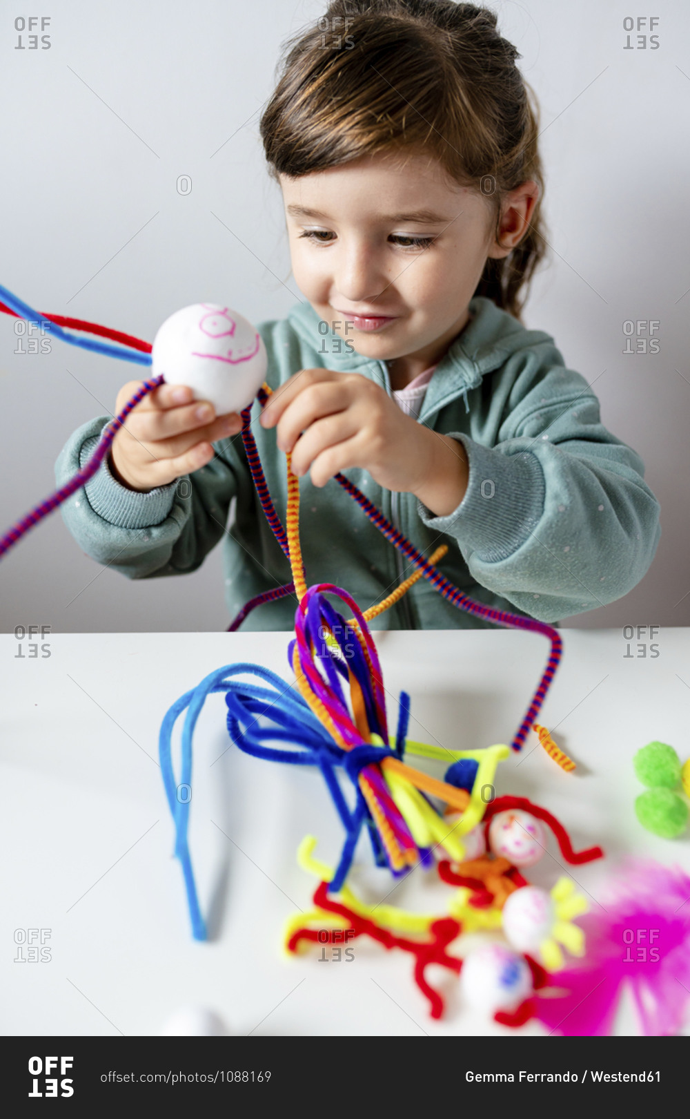Smiling girl making toys of styrofoam ball and pipe cleaners while sitting at home