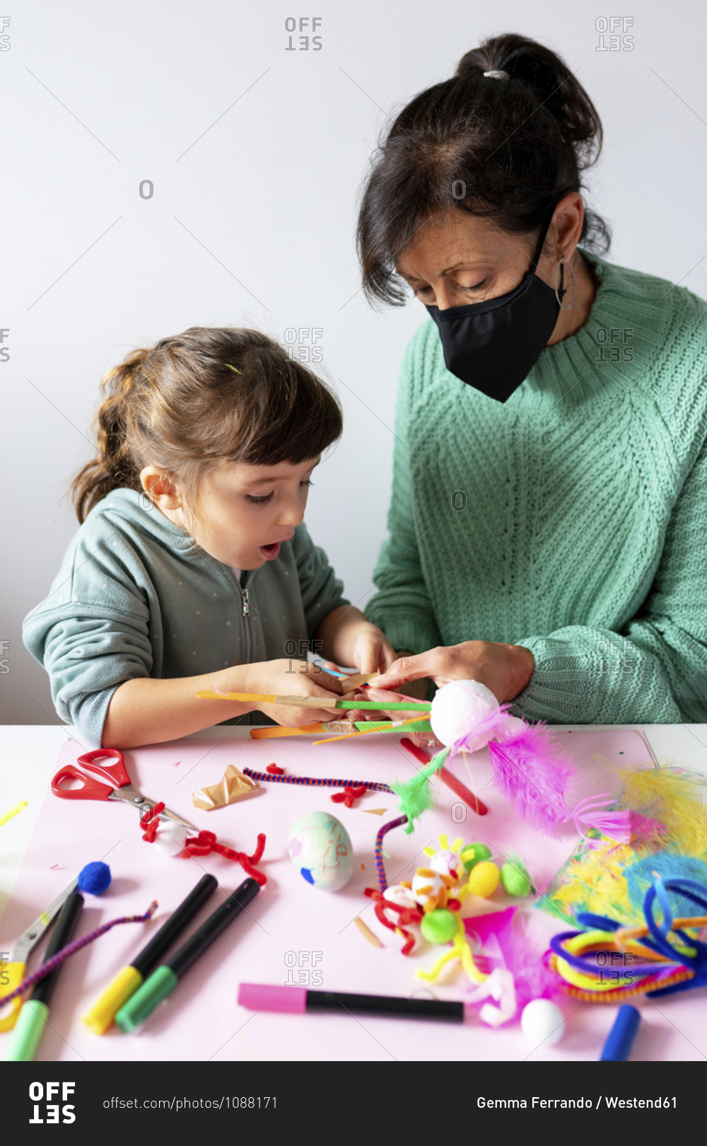 Grandmother and granddaughter making creative toys from pipe cleaners and pom-pom at home during pandemic