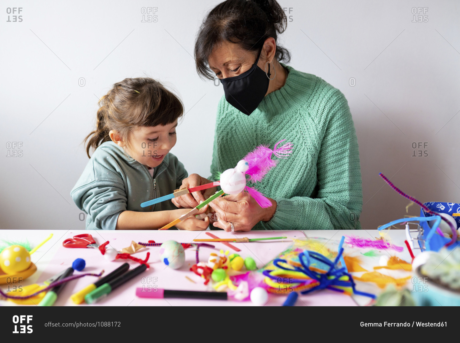 Grandmother and granddaughter making creative toys from pipe cleaners and pom-pom during COVID-19