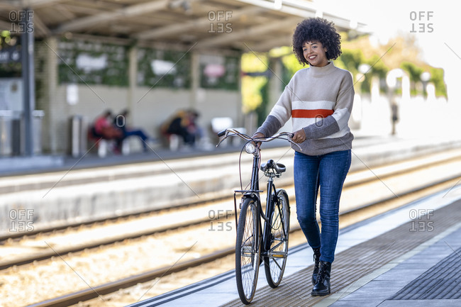 Young woman walking with bicycle while day dreaming at railroad station platform