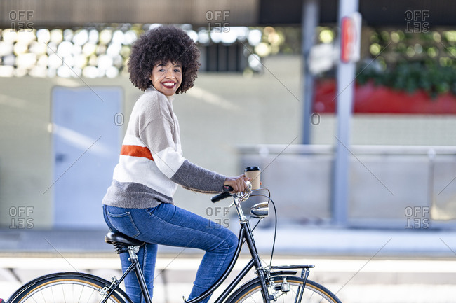 Happy woman looking away while sitting on bicycle at railroad station