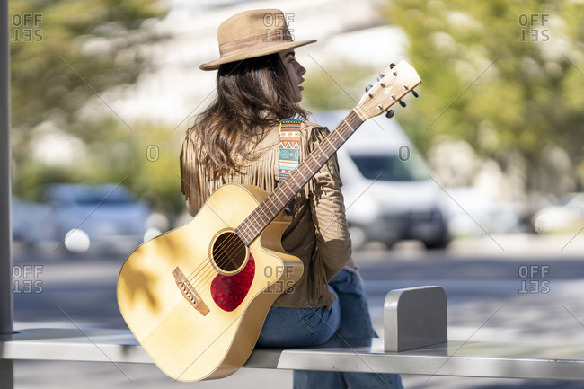 Young woman with guitar sitting at bus stop