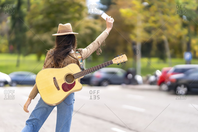 Young woman with guitar waving hand to taxi on street