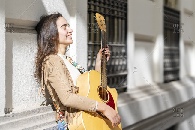 Smiling female musician playing guitar in city on sunny day