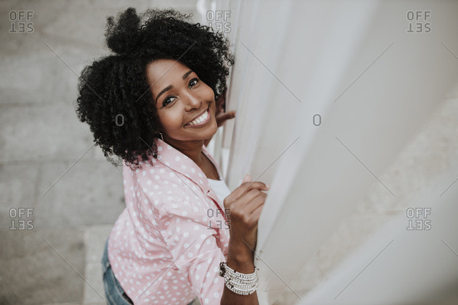 Curly hair woman smiling while leaning on fence