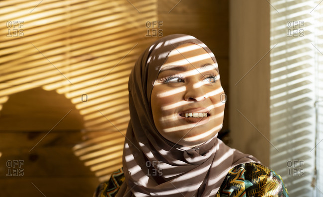 Window blinds shadow on woman face looking away standing at cafe