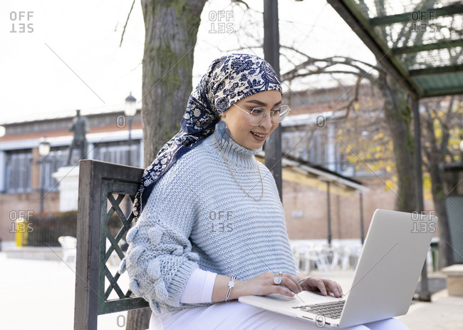 Woman wearing headscarf using laptop while sitting outdoors