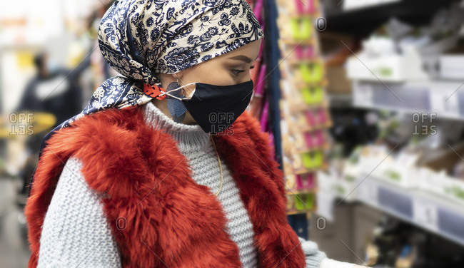 Young woman wearing headscarf and protective face mask shopping while standing at supermarket
