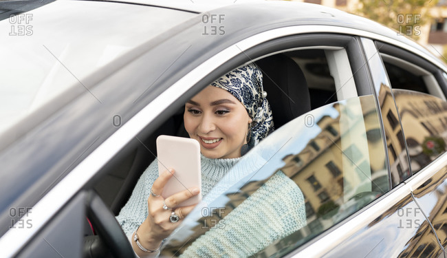 Woman wearing headscarf using mobile phone while sitting in car at city