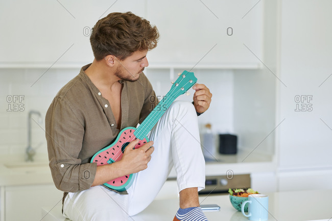 Young man with ukulele sitting over kitchen counter at home