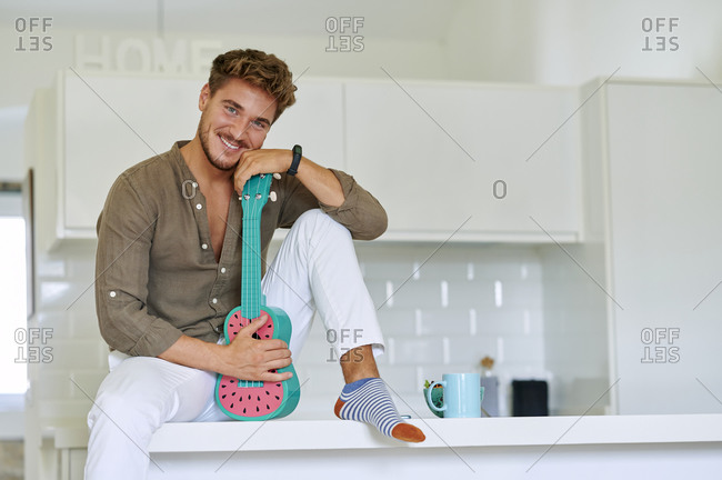 Smiling man sitting with ukulele over kitchen counter at home