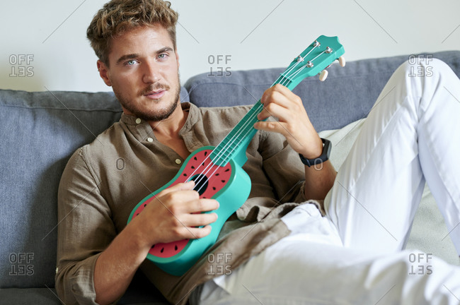 Young man learning ukulele while sitting on sofa in living room
