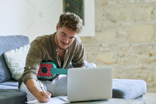 Man learning ukulele through laptop during online tutorial at home