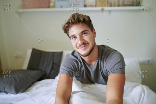 Young man smiling while sitting on bed in bedroom