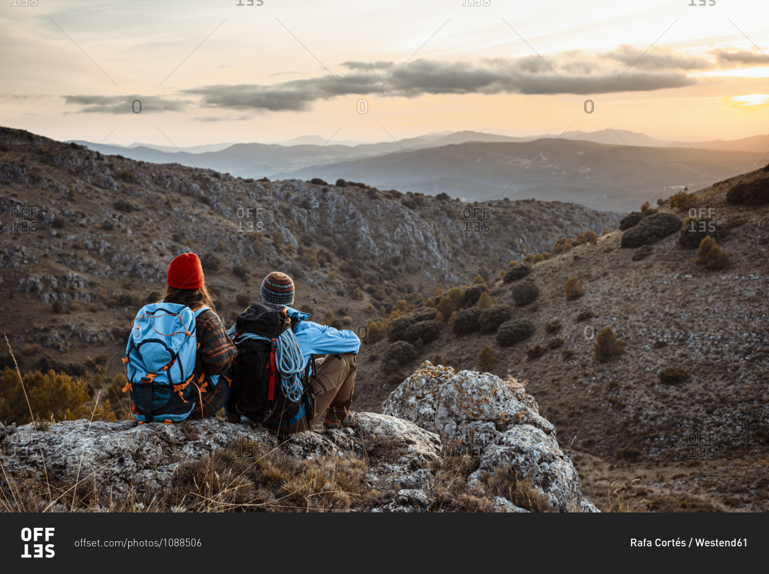Male and female hikers enjoying sunset while sitting on rock mountain during vacation