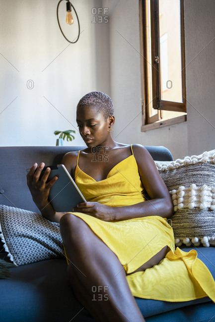 Woman in yellow dress using digital tablet while sitting on sofa at home