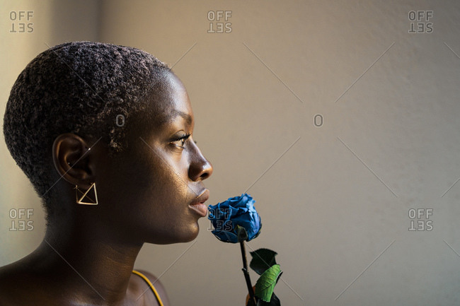 Thoughtful woman with blue rose looking away by white wall