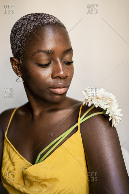 Female hipster with short bleached hair looking at flower on shoulder against white wall