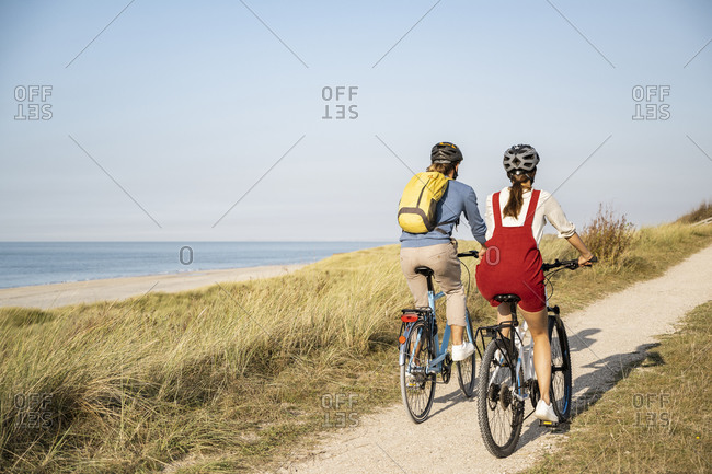 Young couple wearing cycling helmet riding bicycles against clear sky