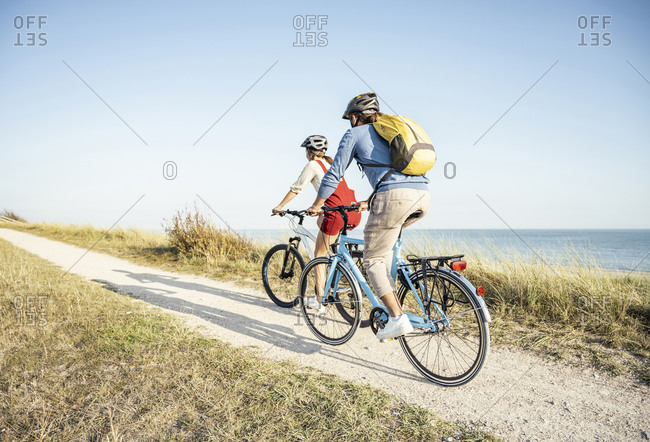 Man with backpack cycling bicycle with woman on footpath during sunny day