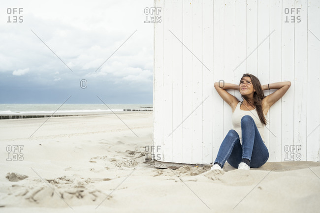 Smiling woman with hands behind head leaning on wall at beach