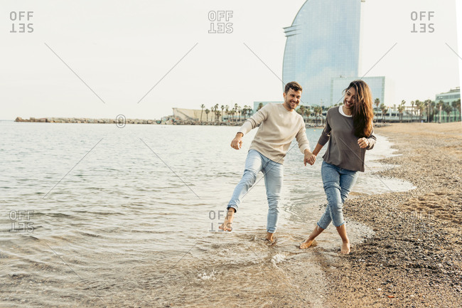 Happy young couple having fun while walking at beach against clear sky