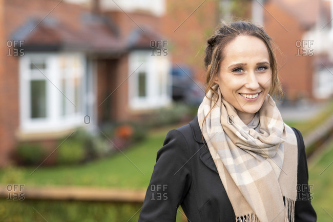 Smiling young woman in scarf standing outside new home