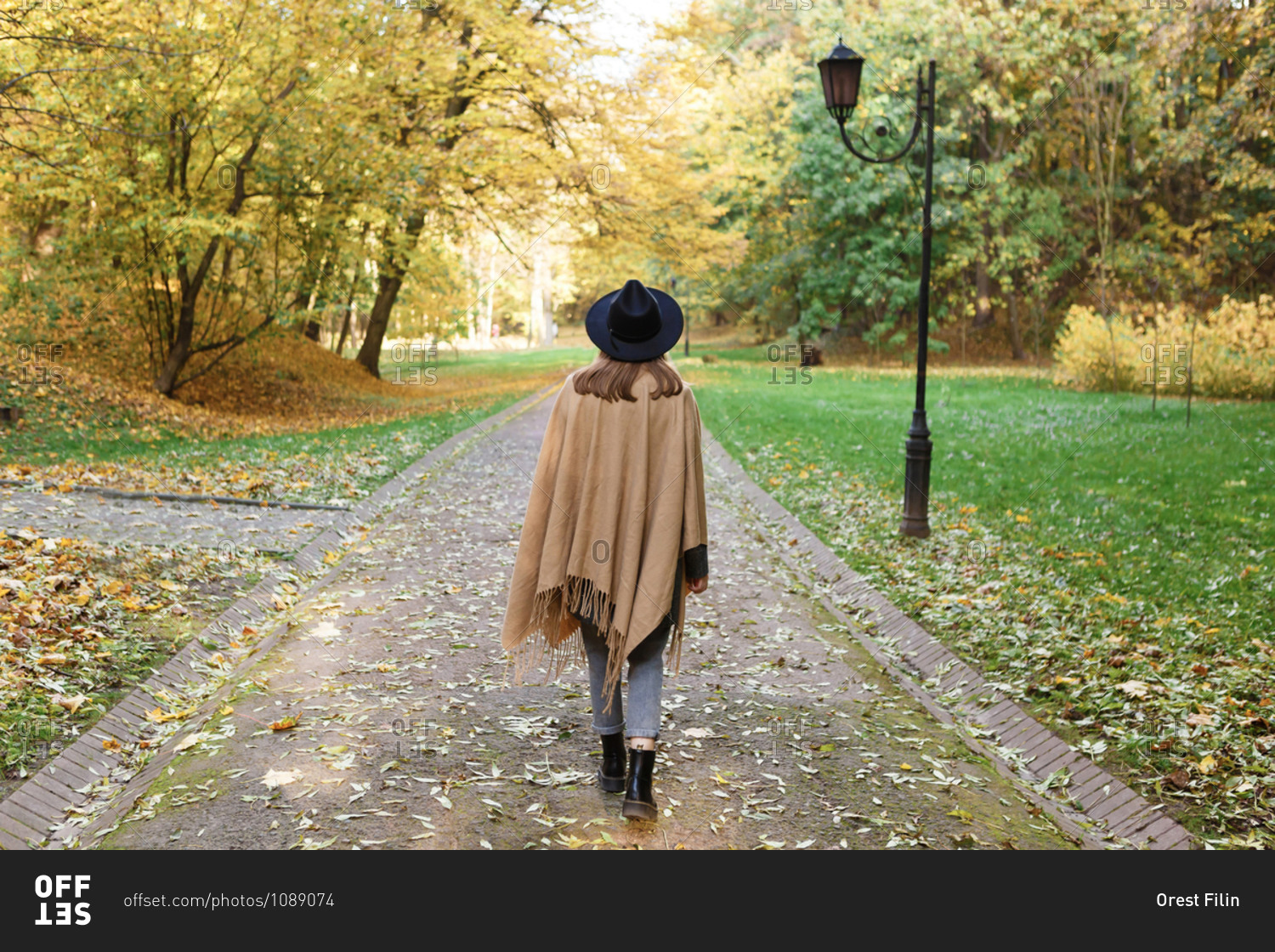 A young woman in a black hat and poncho is walking in the park in the autumn season