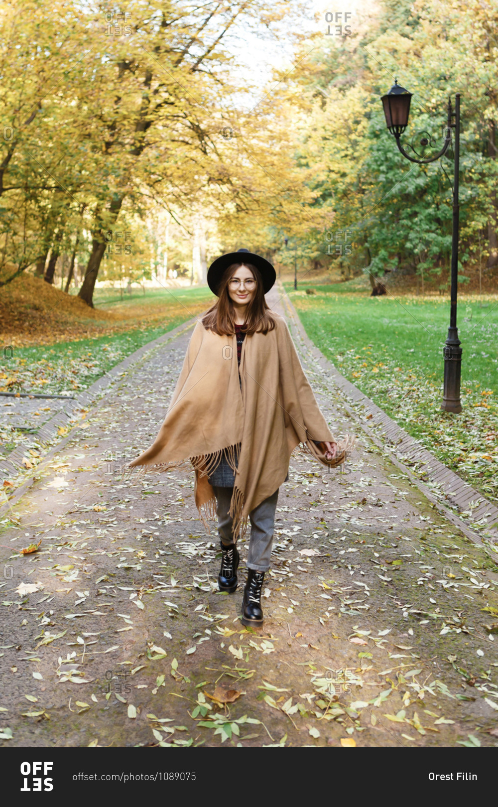 A young woman in a black hat and poncho is walking in the park in the autumn season