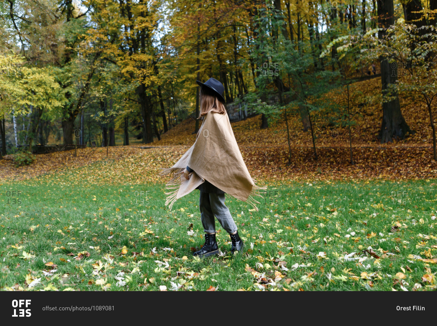 A young woman in a black hat and poncho is dancing on the colorful grass in the park in the autumn season