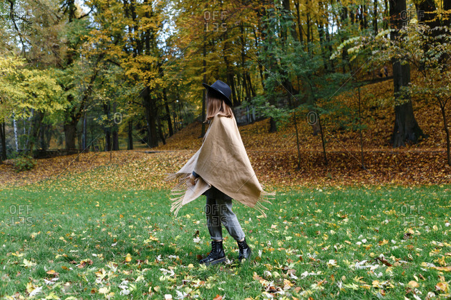 A young woman in a black hat and poncho is dancing on the colorful grass in the park in the autumn season