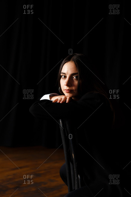 A portrait of an actress woman in formal suit who is sitting on the chair at the stage