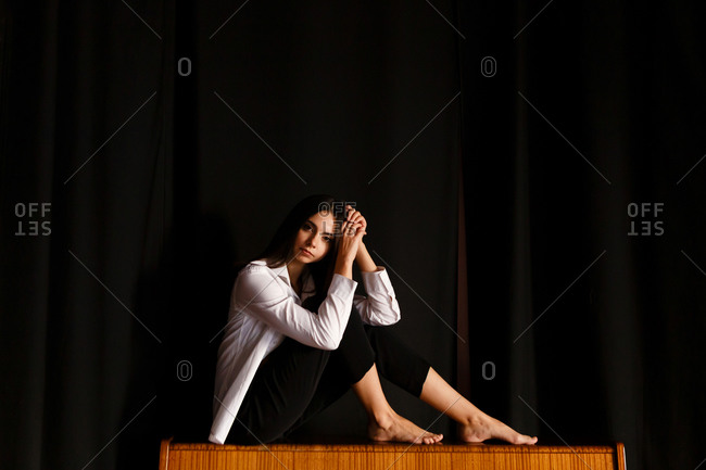 A portrait of an actress woman in formal suit who is sitting on the chair at the stage