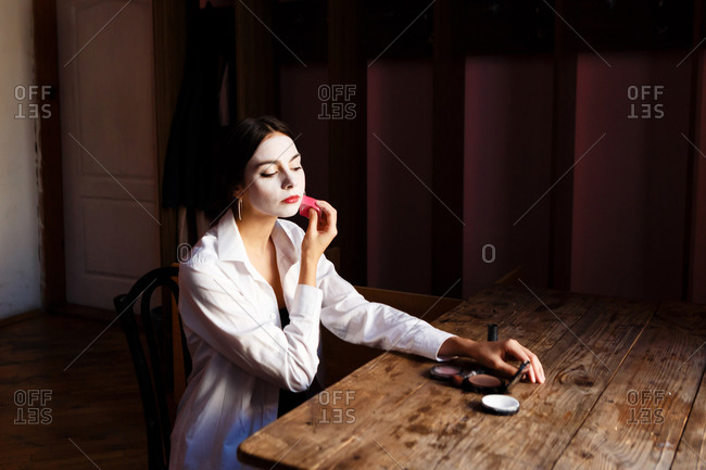 A portrait of an actress woman in a shirt who is sitting on the chair and doing professional theatrical makeup for the stage